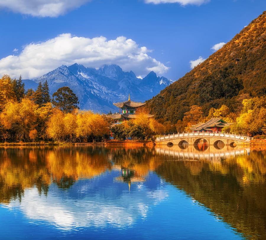 Paisaje de un lago en el bosque con unas montañas de fondo con un cielo azul y unas nubes de la región de Yunnan