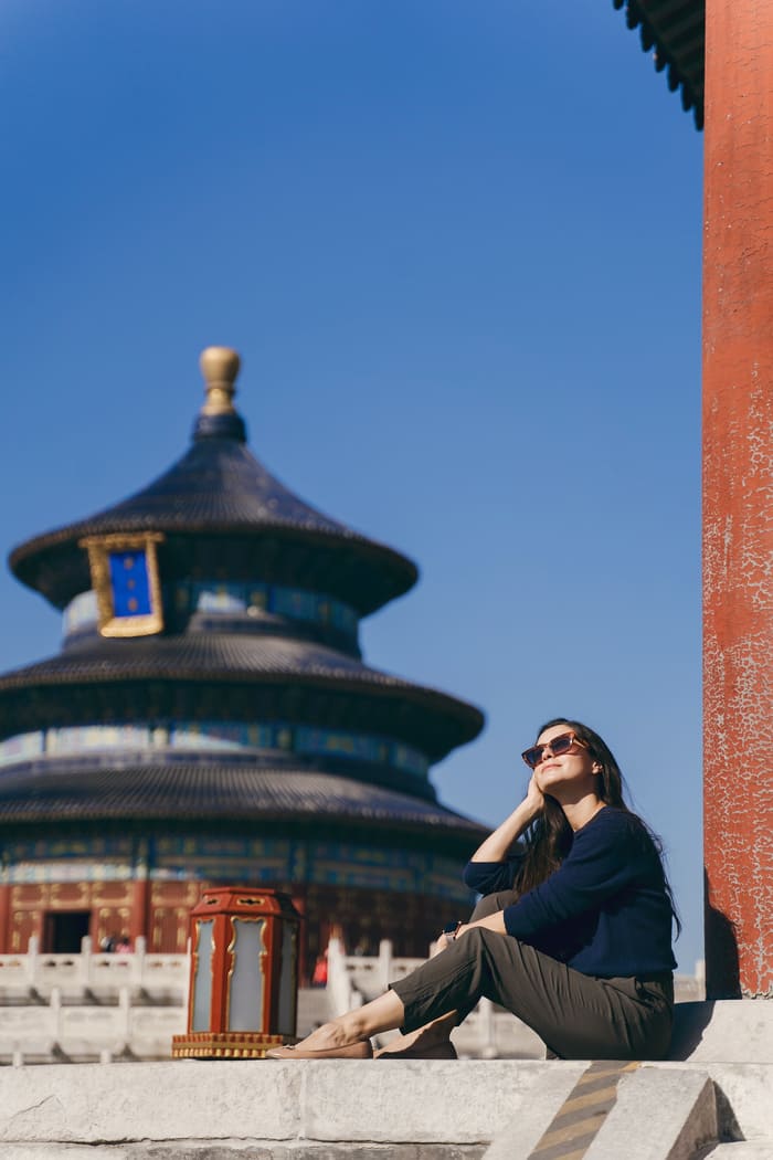 Una chica posando frente e un templo tradicional chino con una columna de color rojo a su derecha y un cielo azul de fondo